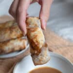 Apple egg rolls being dipped in caramel sauce