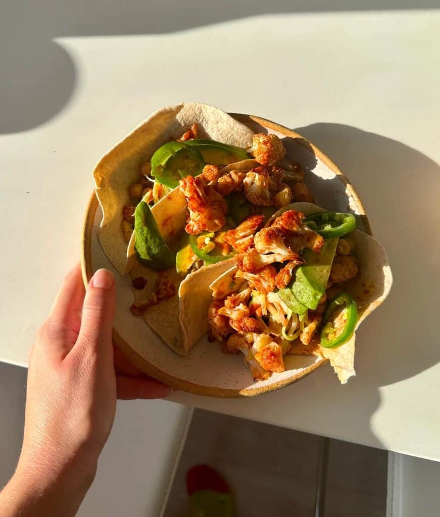 3 tacos in a bowl with cauliflower, avocado, jalapenos and coleslaw.