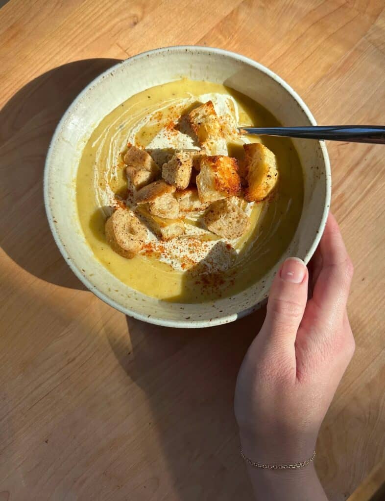 A white speckled bowl with potato leek soup and homemade croutons on top.