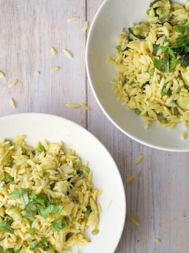 Top down shot of two bowls of lemon orzo with peas and topped with basil.