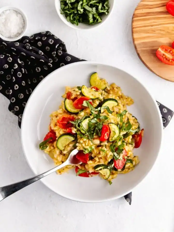 A bowl of creamy risotto topped with zucchini and tomatoes.
