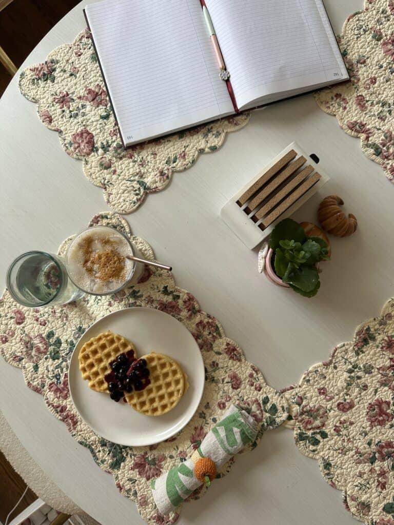 A top down shot of a kitchen table with waffles and coffee and an open journal