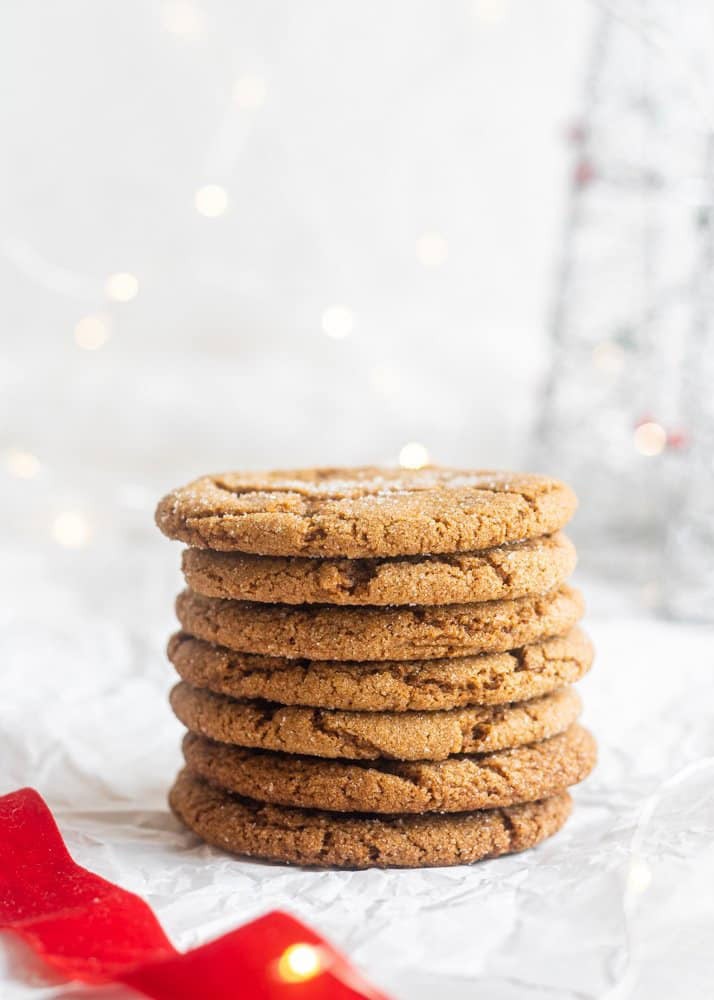 A stack of seven ginger cookies on a piece of white parchment paper with string lights in the background.