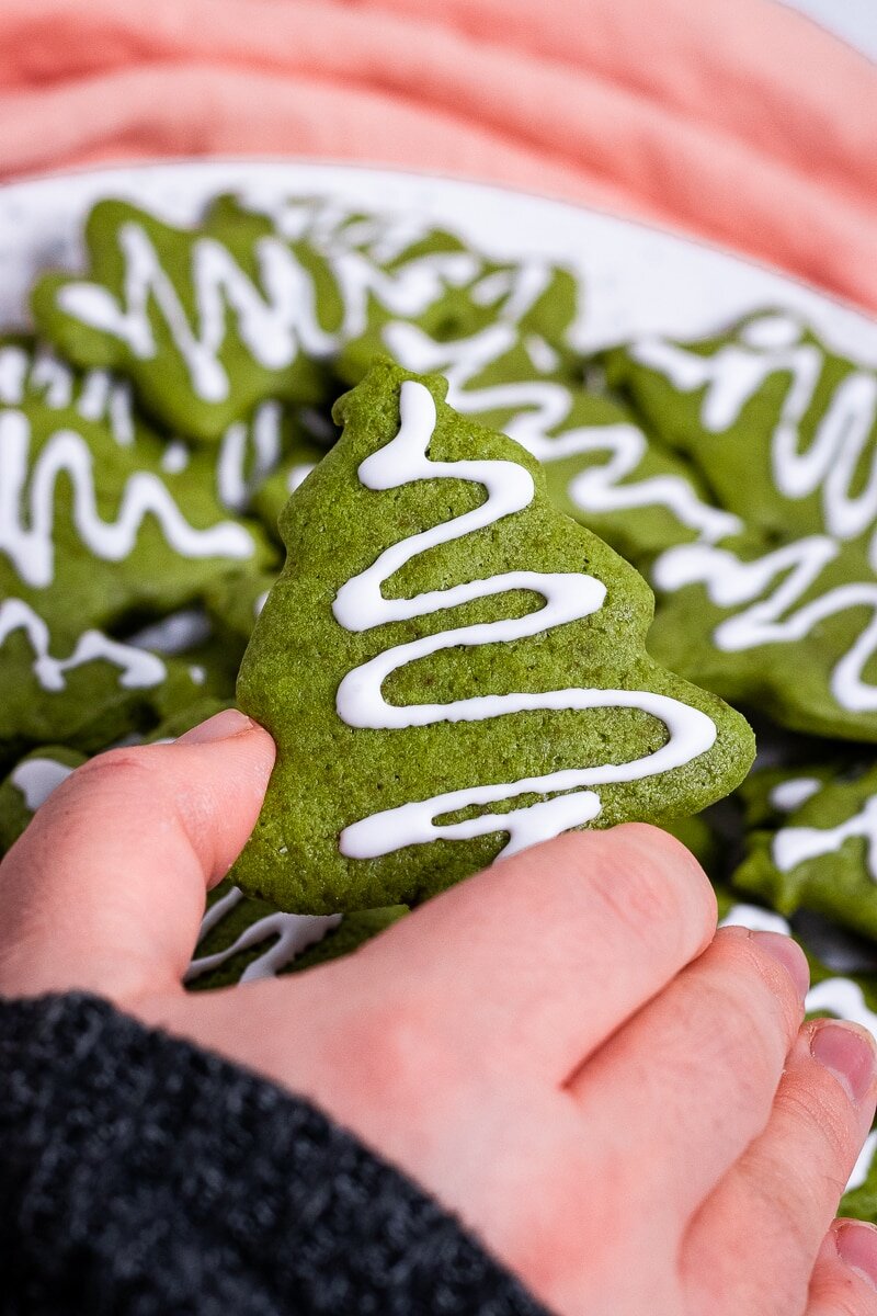 Green christmas cookies with icing on them and a hand holding them.