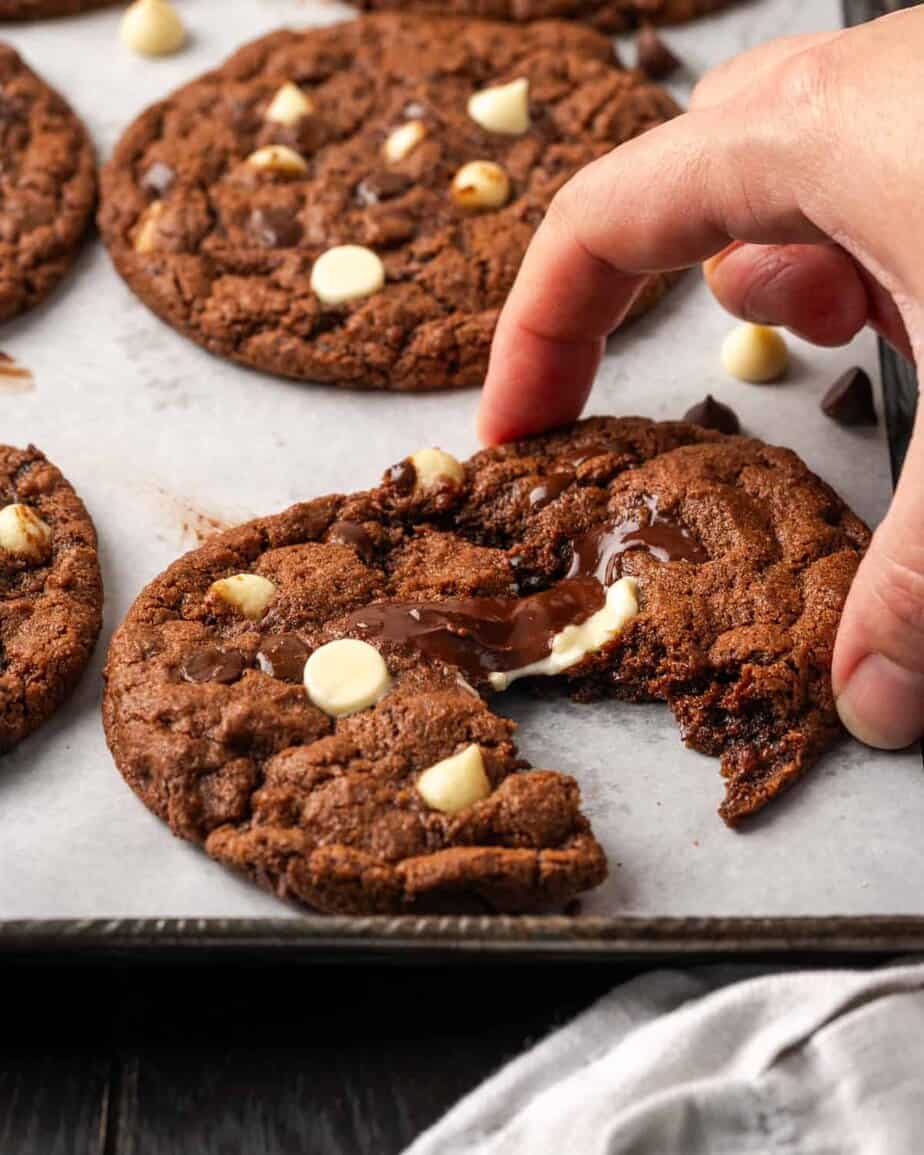 A hand pulling apart chocolate cookies on a baking tray.