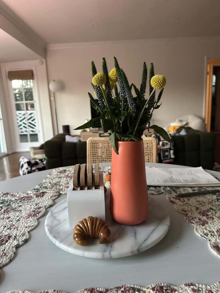 A kitchen table with coasters and fresh flowers.