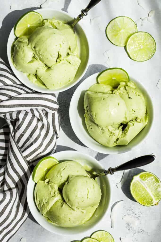 A top down shot of three bowls of vibrant green ice cream with limes scattered nearby