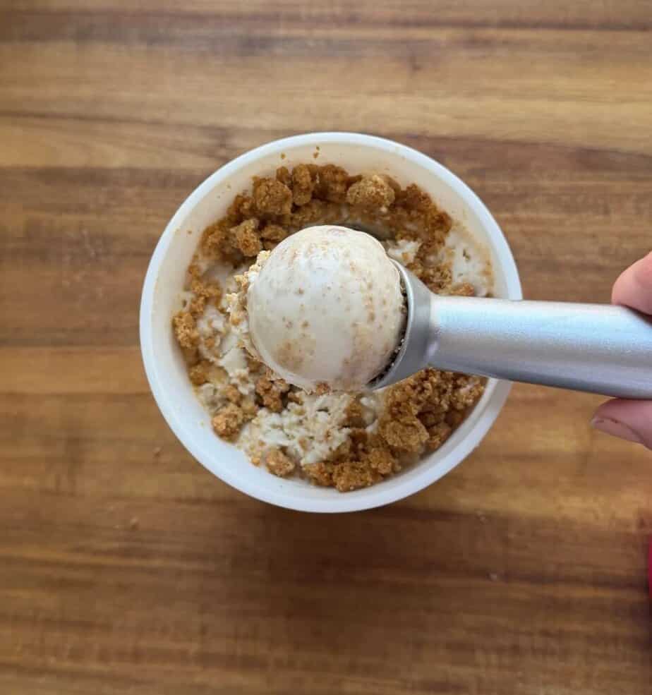 An ice cream container in the background with a scoop of ice cream at the forefront.