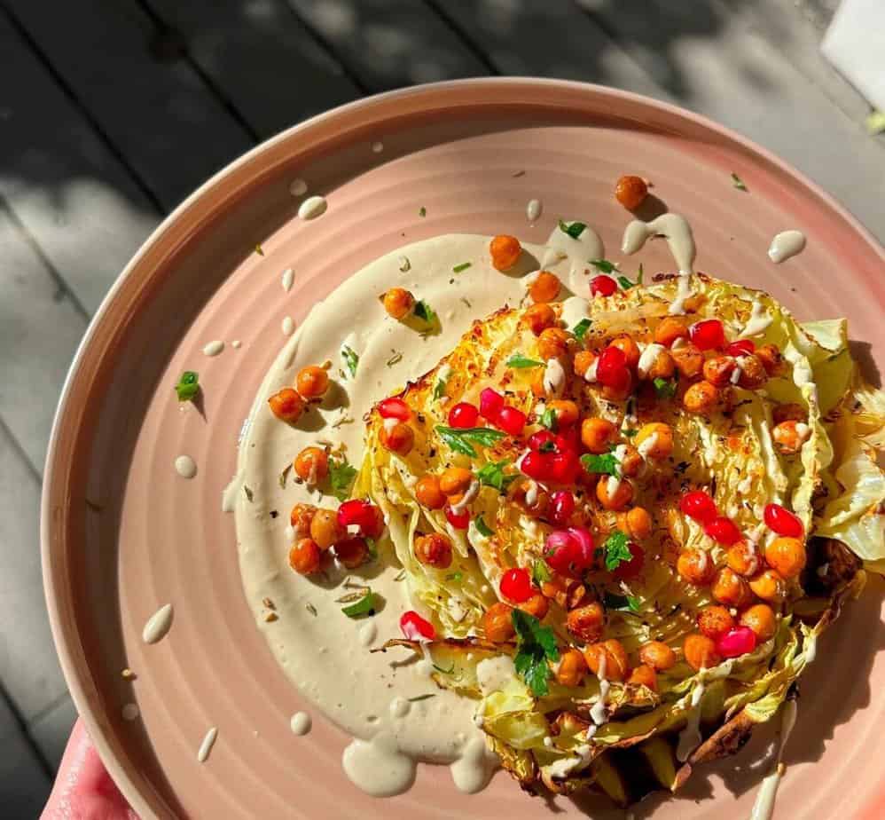 A slice of cabbage topped with pomegranates and chickpeas