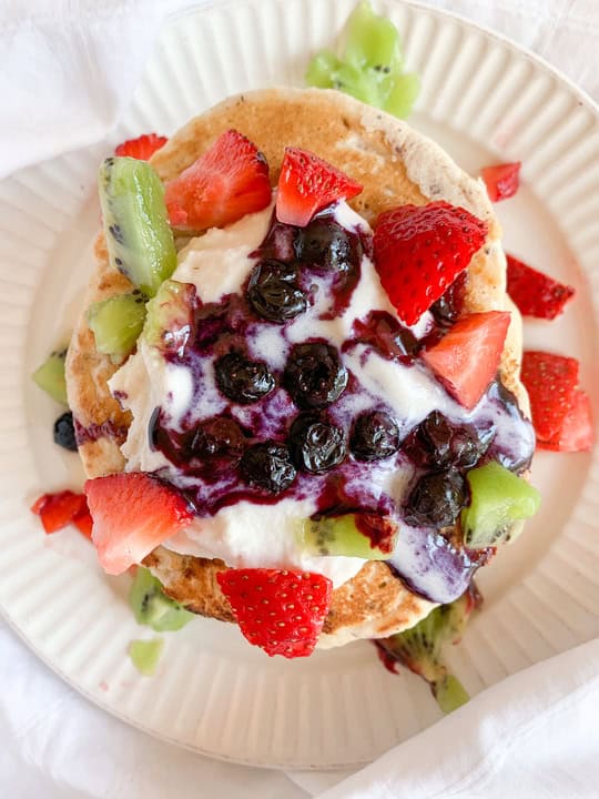 A top down shot of pancakes topped with strawberries, blueberries, and kiwis