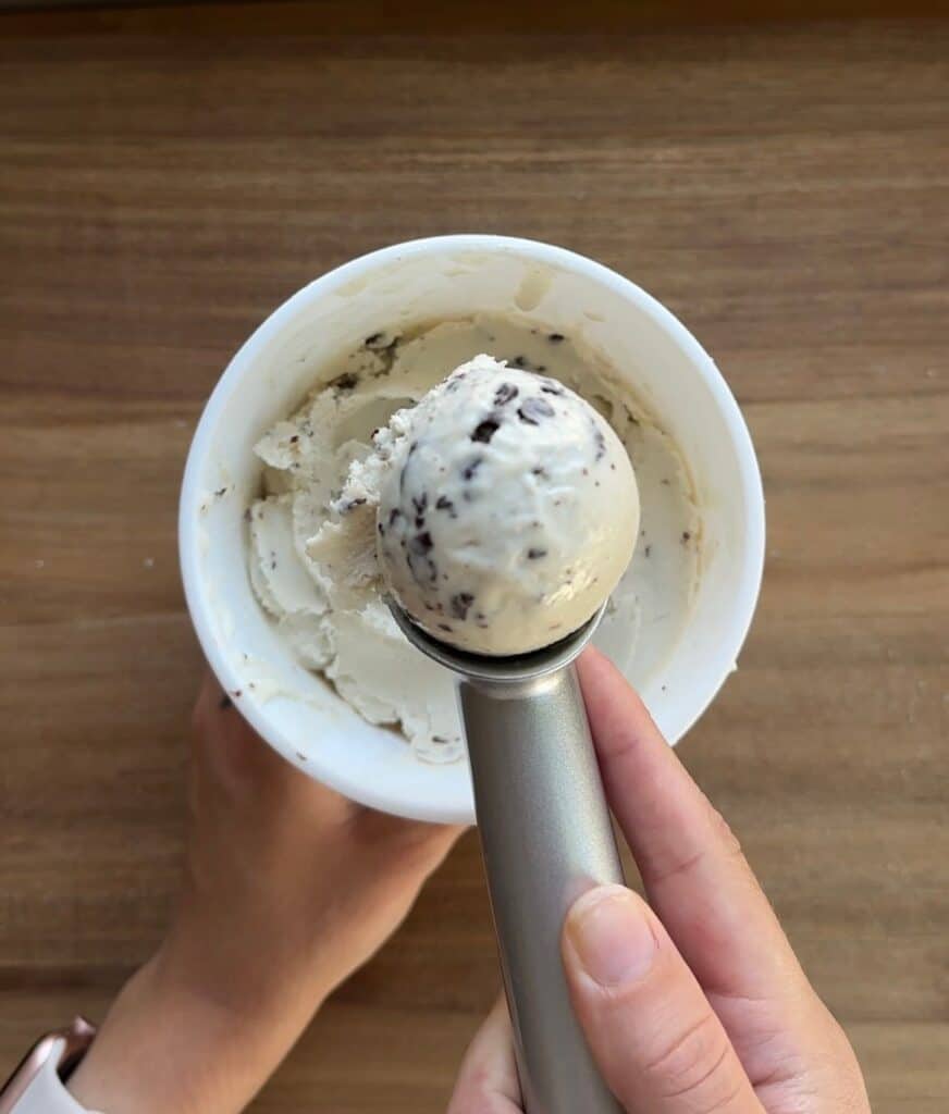 A scoop of mint chocolate chip ice cream in the forefront with the container in the background.