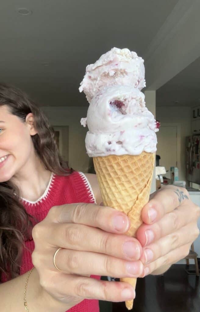 A girl holding a cone with three scoops of ice cream in it with cherry chunks