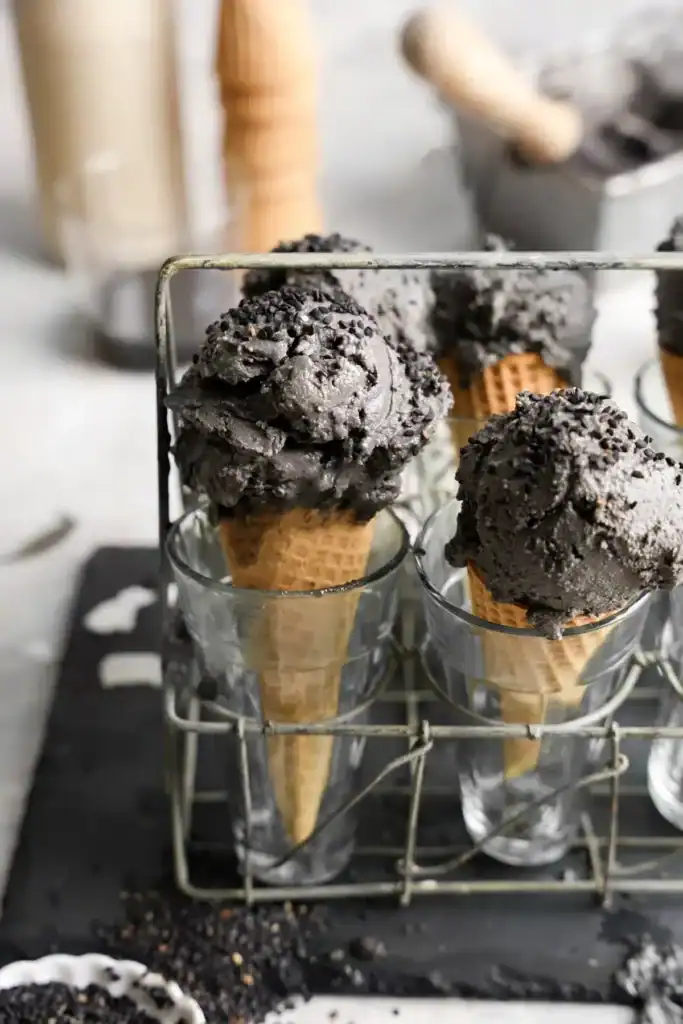 Multiple cones topped with black sesame ice cream in individual glass cups stacked in a carrying case