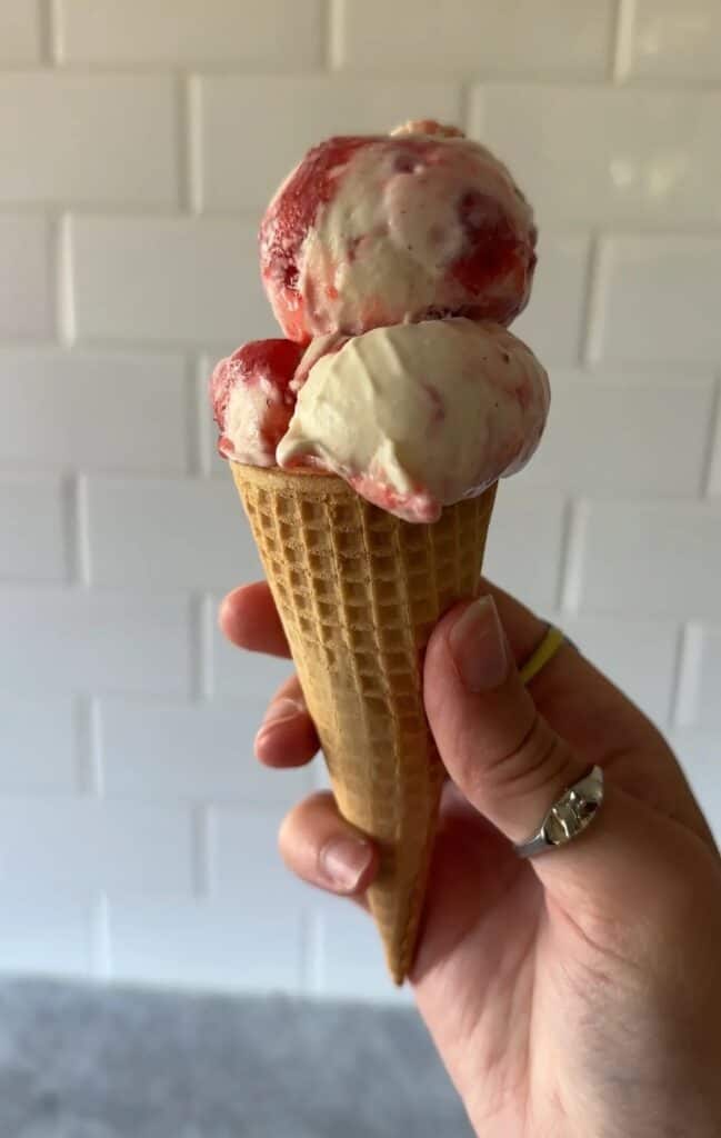 A hand holding a cone of corn and strawberry swirled ice cream