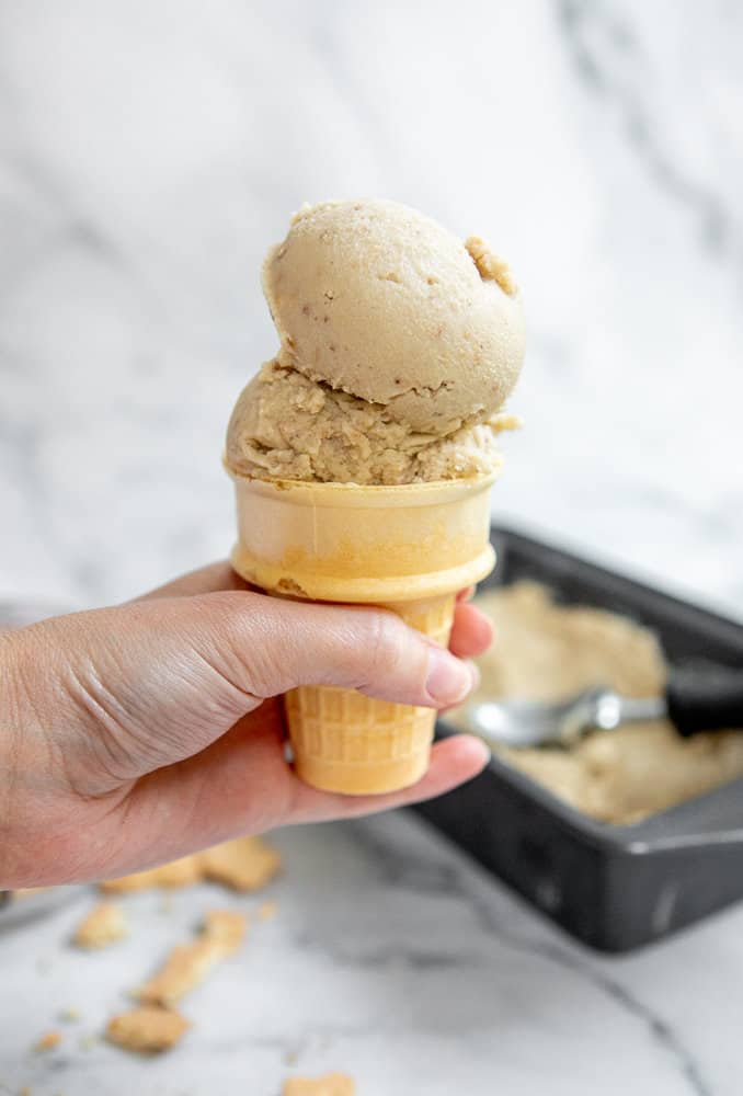 A hand holding a cone of banana pudding ice cream with the container in the background