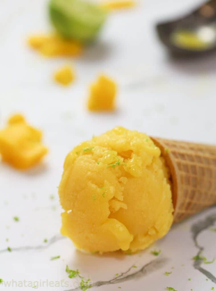 An ice cream cone with mango ice cream laying on it's side with specks of lime on top of it and by the side