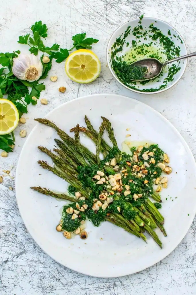 Top down shot of asparagus topped with a hazelnut gremolata and surrounded by cilantro, garlic, and lemon