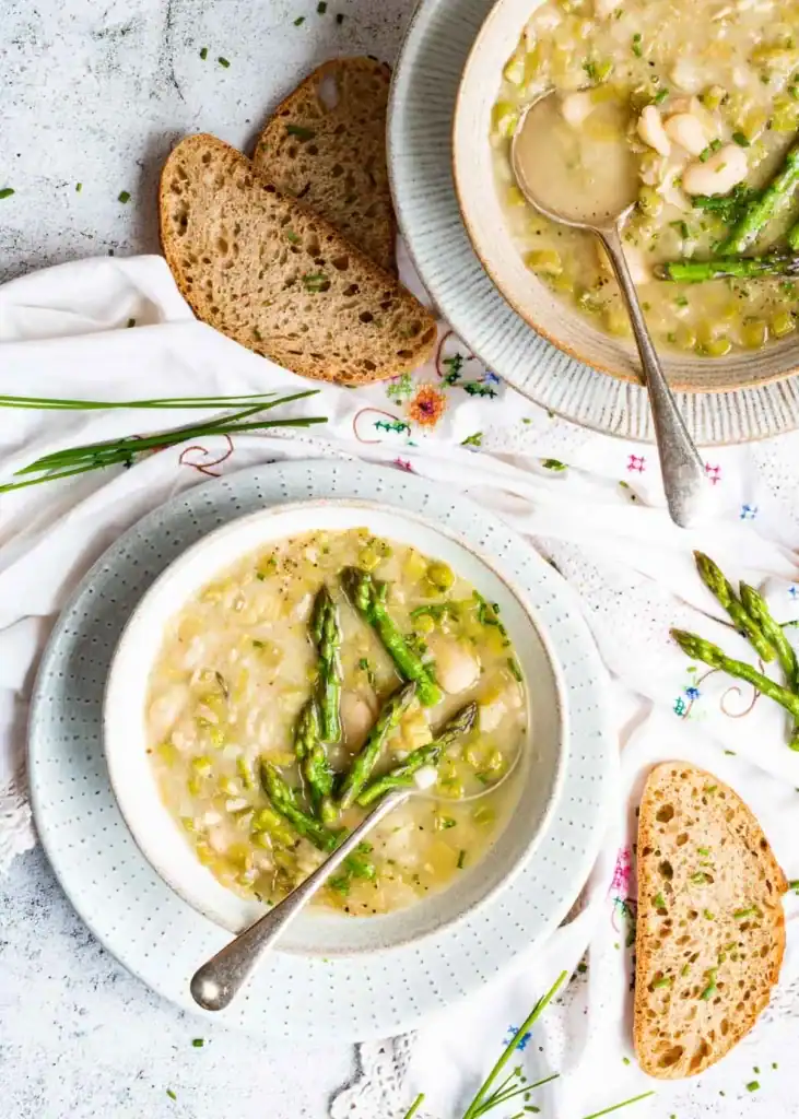 Top down shot of two bowls of soup made with white bean and leeks and topped with asparagus
