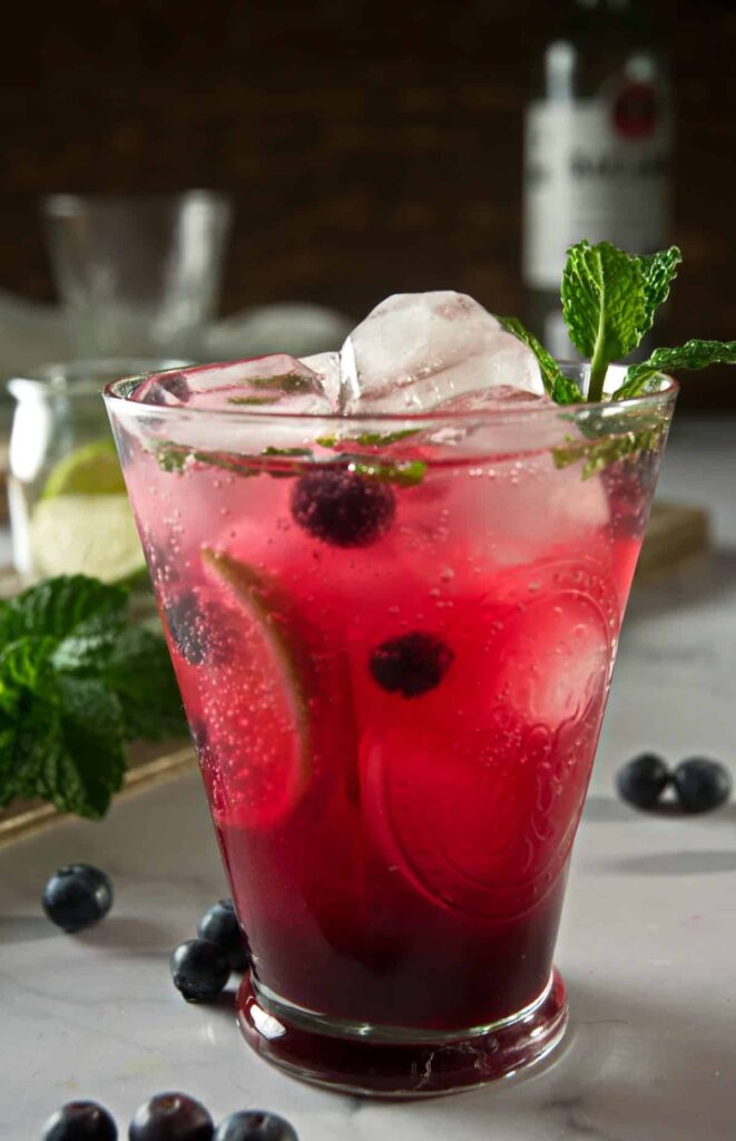 A blueberry mojito mocktail with fresh blueberries and limes inside and garnished with mint