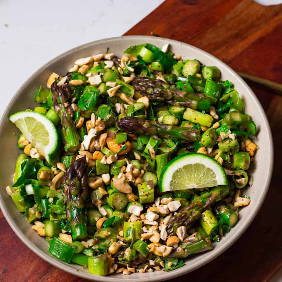 Bowl filled with asparagus, cashews, ginger, garlic, and finished with slices of lime.