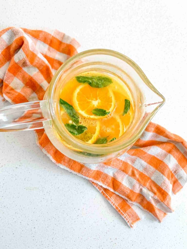 Top down shot of a jug of non-alcoholic mint julep punch on an orange plaid towel