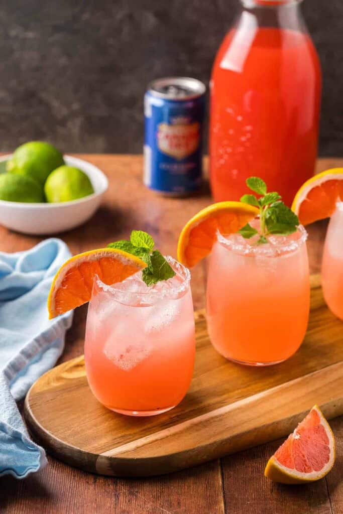 A row of paloma mocktails garnished with orange and mint