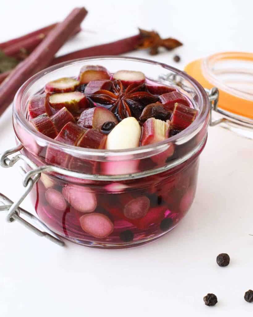 A close up of pickled rhubarb in a glass jar topped with star anise. 