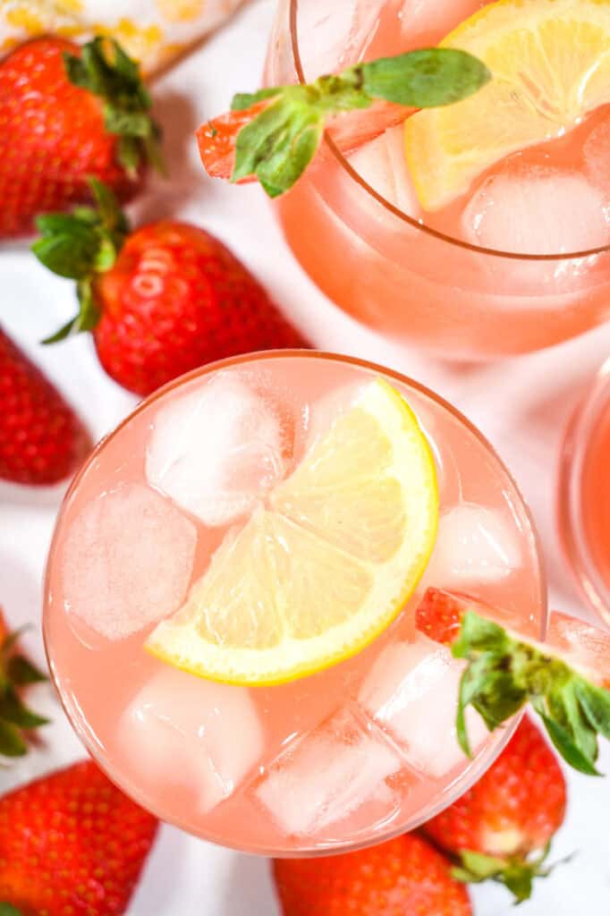 Top down shot of a glass of rhubarb lemonade with a slice of lemon on top and strawberries scattered nearby.
