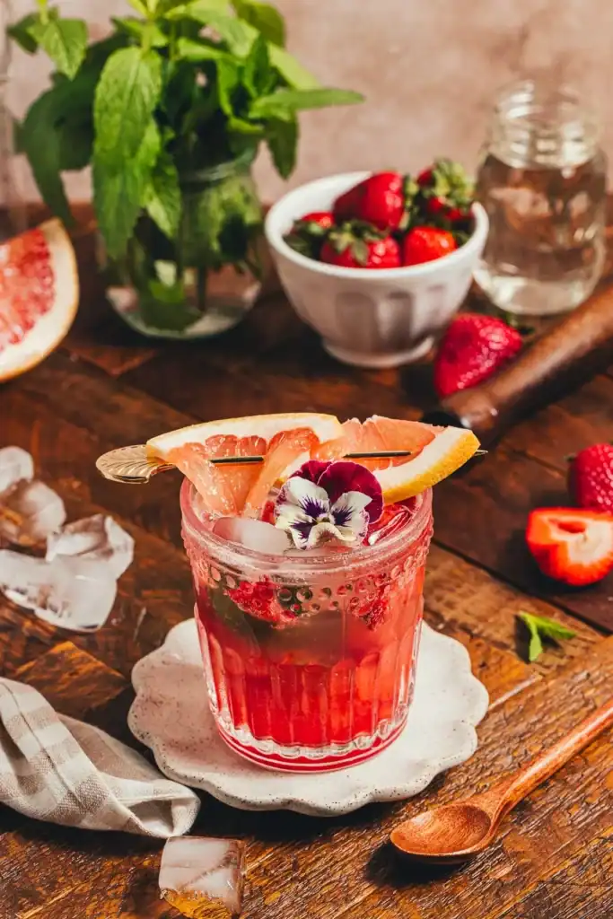 A strawberry grapefruit mocktail with orange slices on top and garnished with flowers