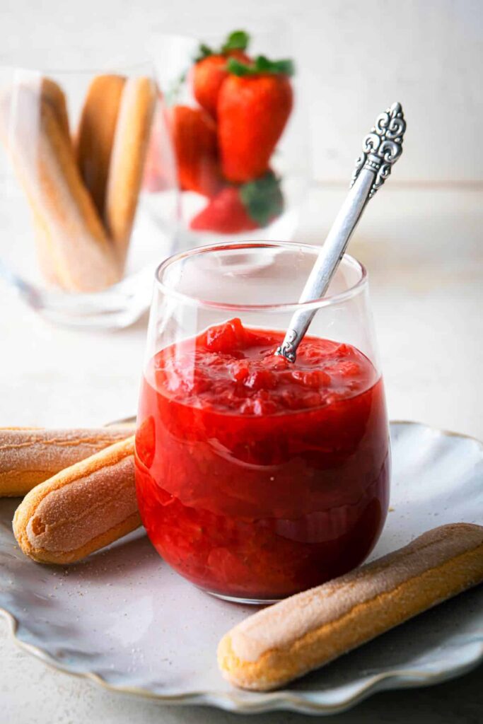 A glass filled with strawberry rhubarb sauce and surrounded by ladyfinger cookies. 