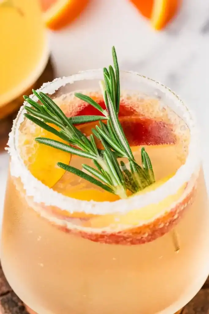 An extreme close up of a white sangria mocktail garnished with fruit and rosemary