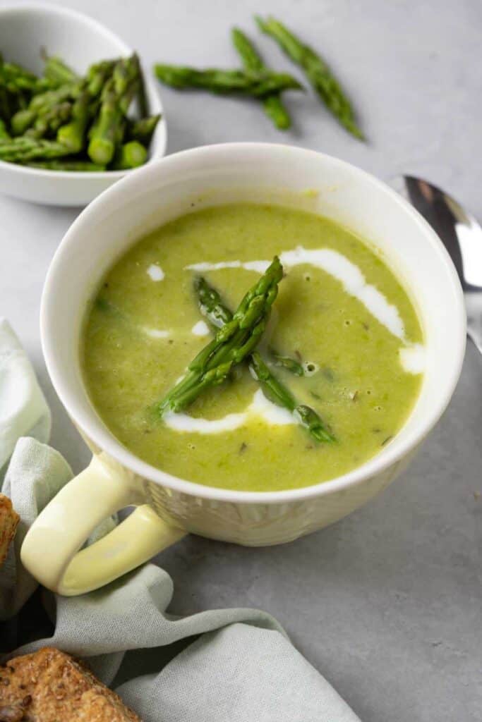 A mug of asparagus potato soup topped with asparagus 