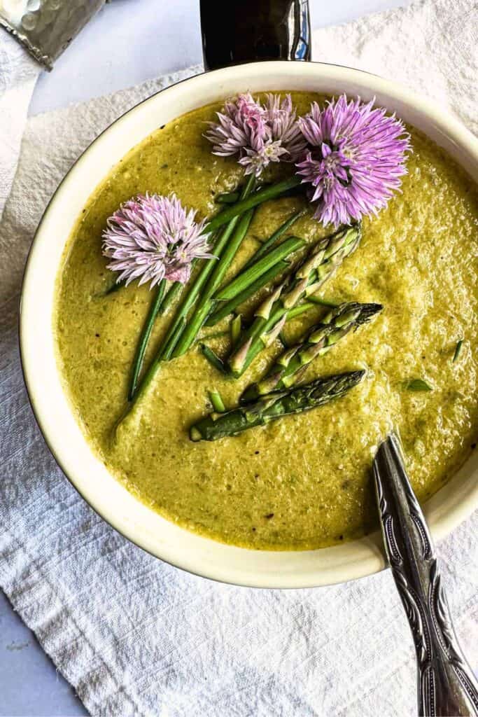 Top down shot of asparagus soup topped with asparagus and purple flowers