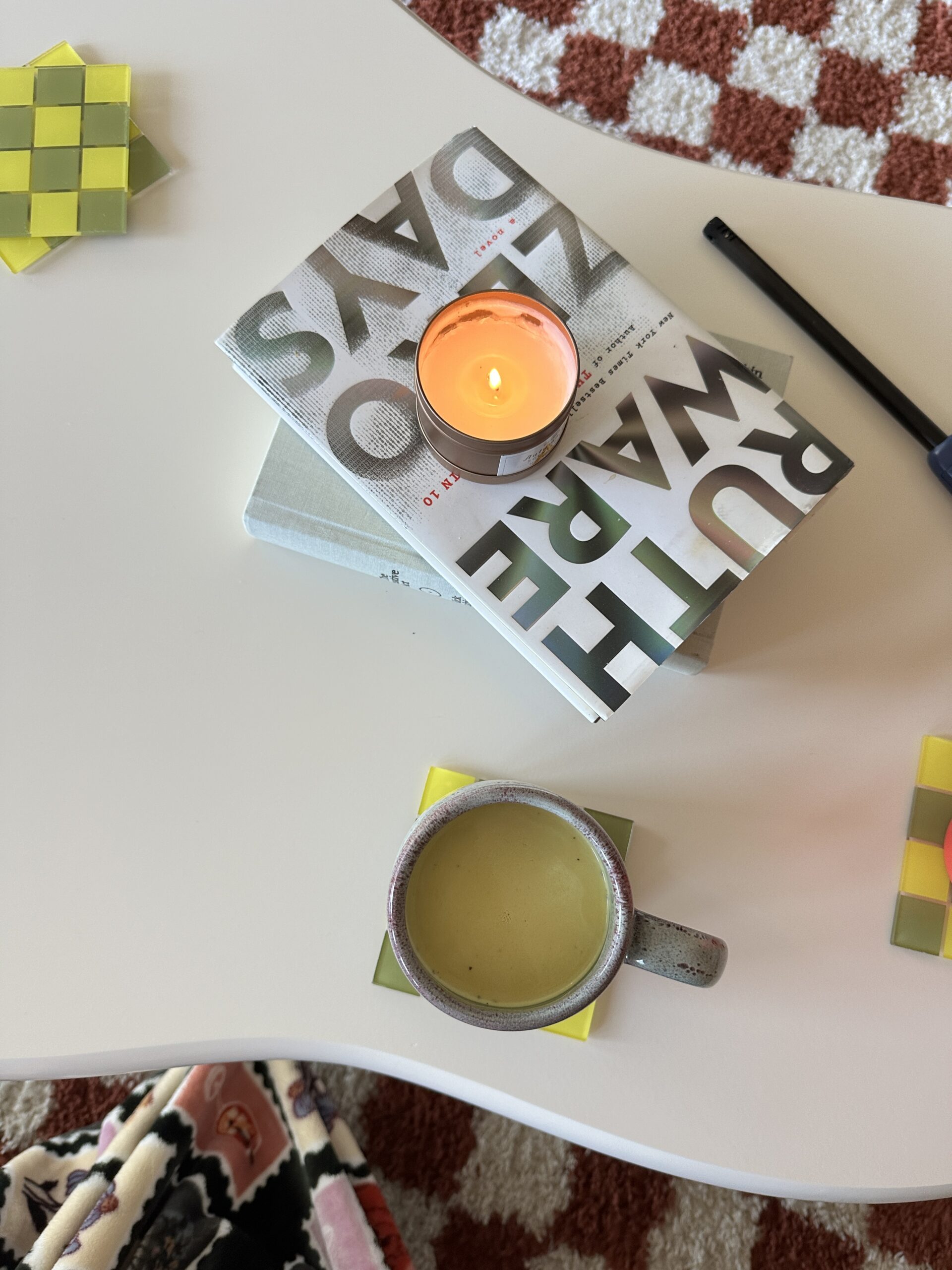 A coffee table with a warm drink, a stack of books, and a lit candle