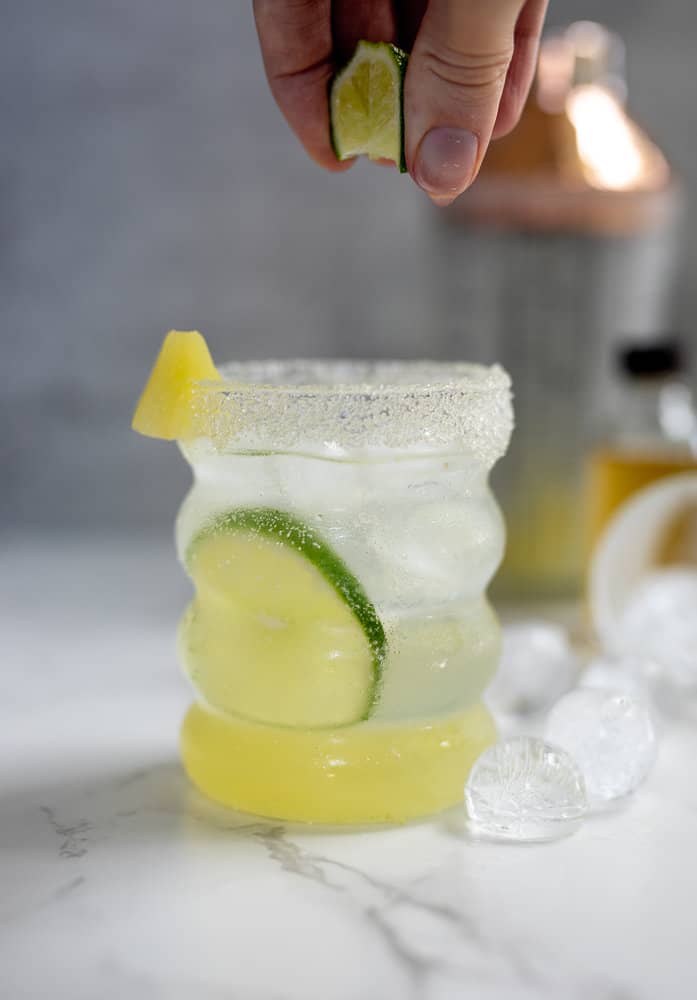 A lime being squeezed into a pineapple ginger mocktail