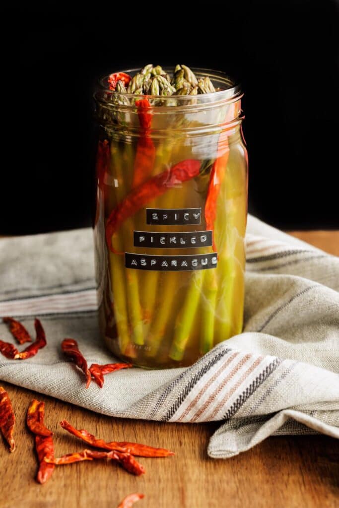Pickled asparagus in a jar with chili peppers and with a label that says 'spicy pickled asparagus;