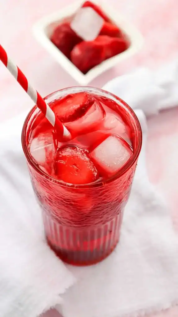 Close up of a strawberry acai refreshed in a glass cup with a red and white striped straw