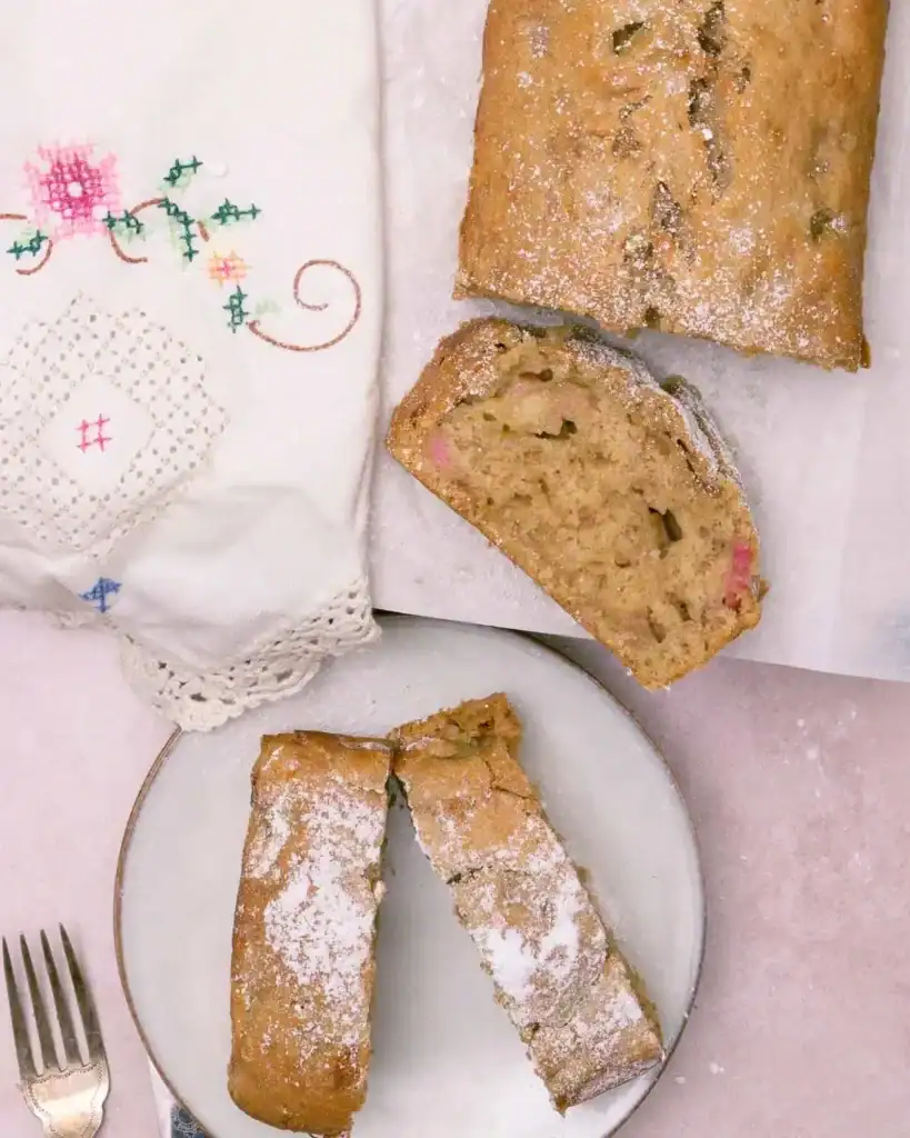 A top down shot of rhubarb banana bread with two slices on a white plate next to it
