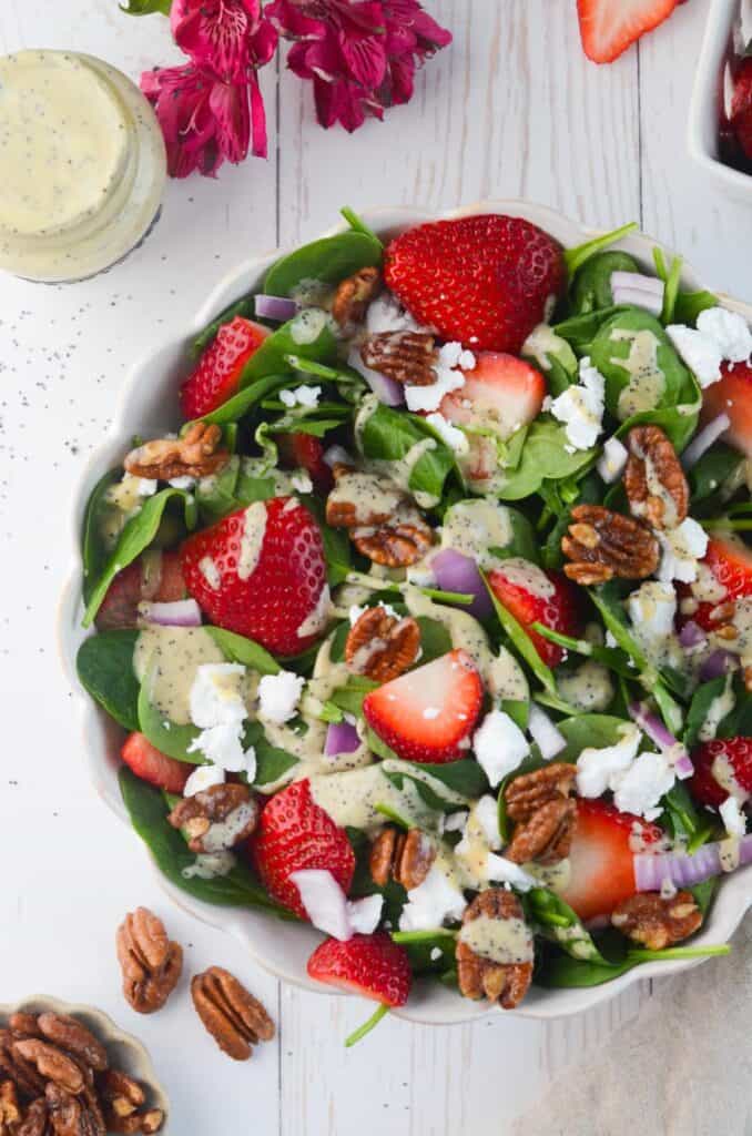 Top down shot of a spinach salad with strawberries, pecans, red onion, and more.