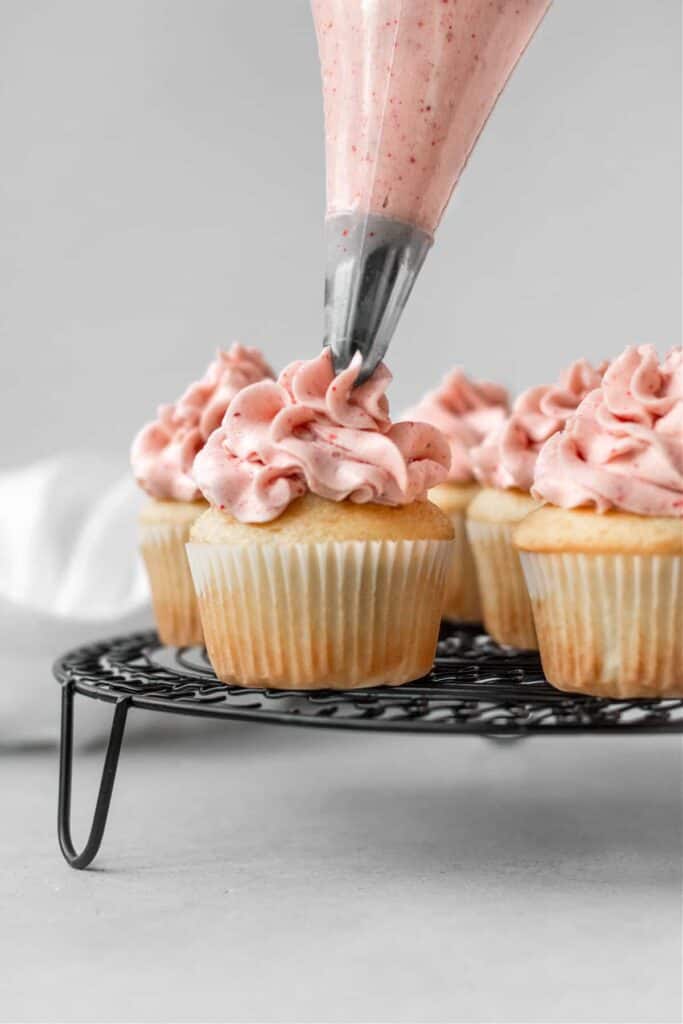 Piping on top of vanilla cupcakes strawberry frosting