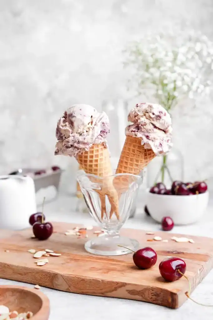 A glass container with two ice cream cones and scoops of almond cherry ice cream