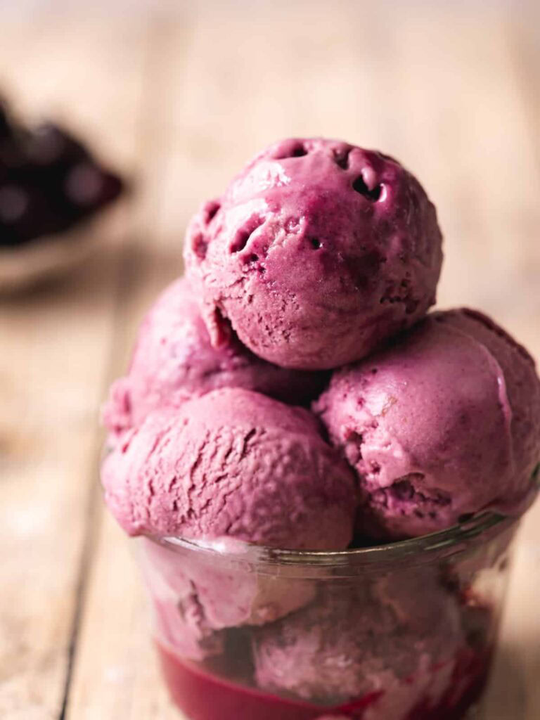 A container of vegan black cherry ice cream with multiple scoops on top
