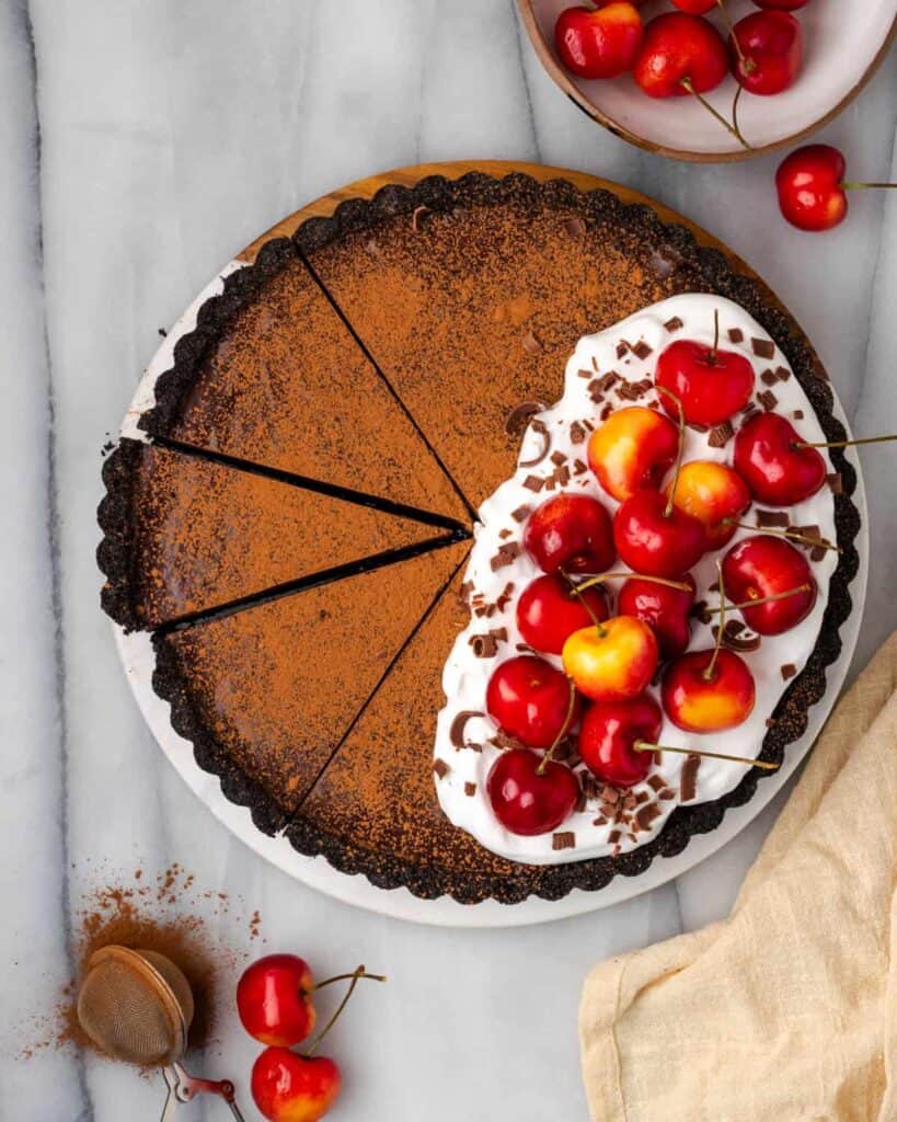 A top down shot of a no bake chocolate ganache tart topped with whipped cream, chocolate and cherries