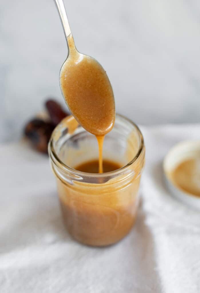 Date caramel dripping off a spoon and into the jar.