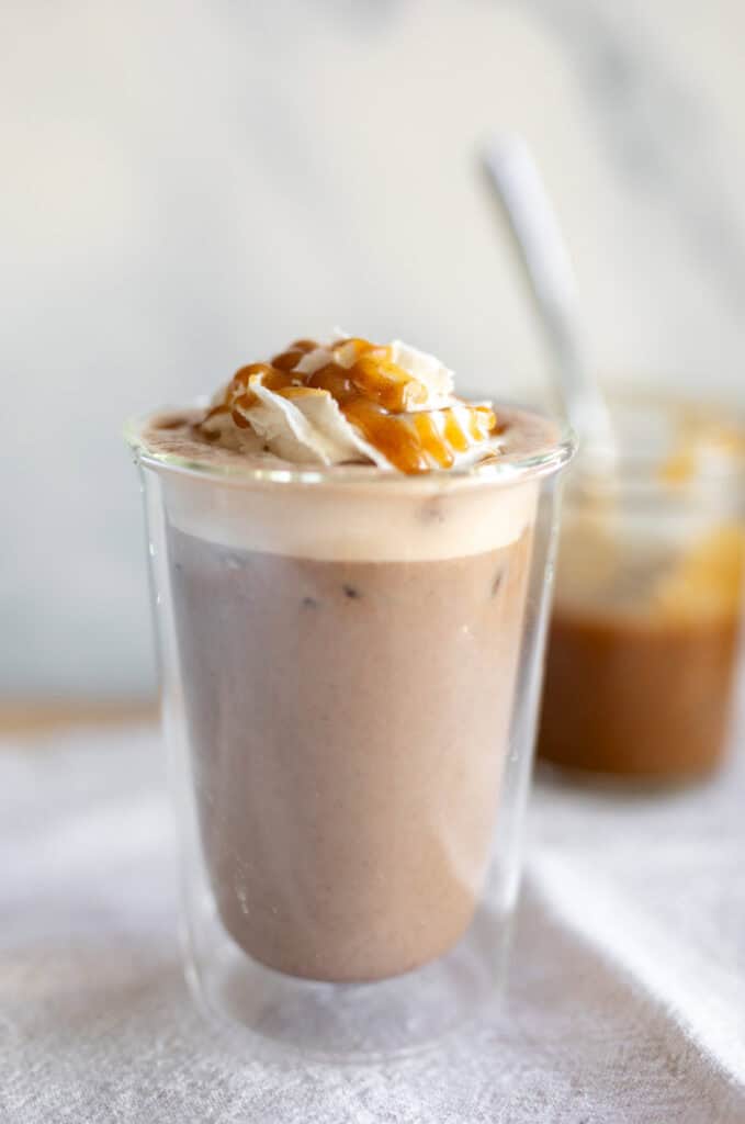 A date latte with a drizzle of date caramel on top and a jar of date caramel in the background.